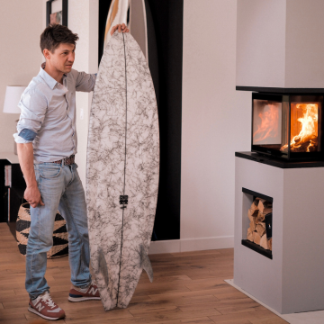 Gautam montre ses planches de surf devant le poêle à bois insert Aäsgard en feu